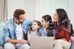 Family smiling and using laptop on sofa