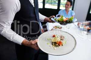 Portrait of waiter standing with meal next to customers