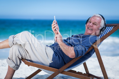 Mature man resting on a deck chair listening to music with smart