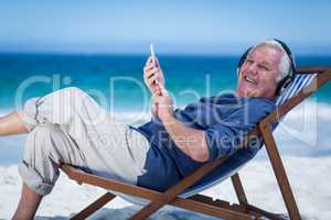 Mature man resting on a deck chair listening to music with smart