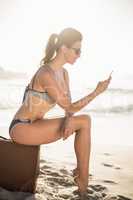 Glamorous woman in bikini sitting and using mobile phone
