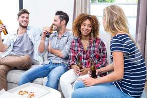 Friends enjoying beer while sitting on sofa at home
