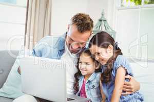 Father and daughters looking in laptop at home