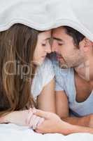 Close-up of couple romancing under blanket on bed