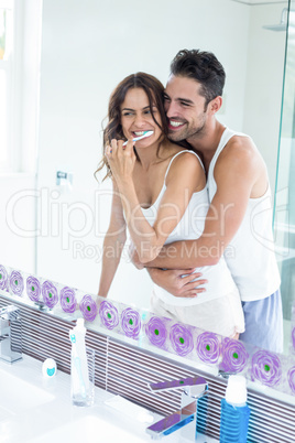 Reflection of wife brushing teeth while husband embracing her