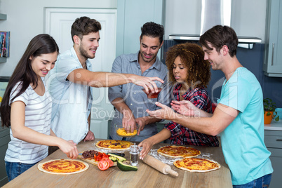 Multi-ethnic friends preparing pizza on kitchen table