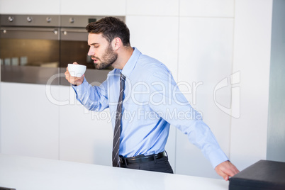 Businessman drinking coffee while standing by table