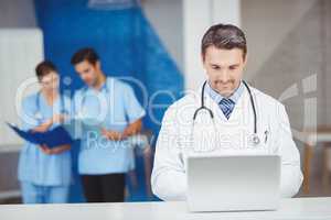 Doctor working on laptop with colleagues discussing
