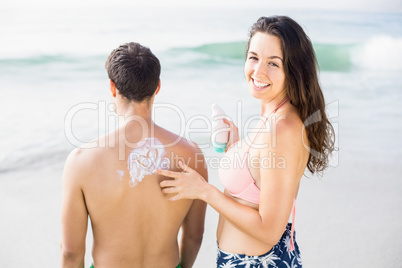 Woman making a heart symbol on mans back while applying a sunscr