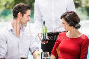 Midsection of waiter showing wine bottle to couple