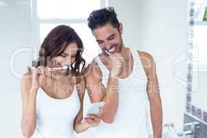 Couple looking in mobile phone while brushing teeth