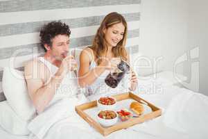 Smiling couple having breakfast on bed