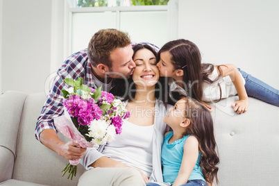 Father and daughter kissing mother sitting on sofa