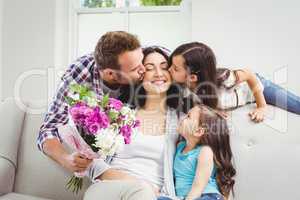Father and daughter kissing mother sitting on sofa