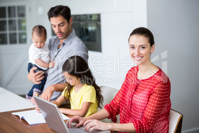 Smiling mother working on laptop with father helping daughter in