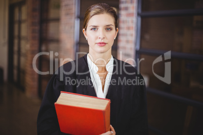 Confident female lawyer with book standing in office