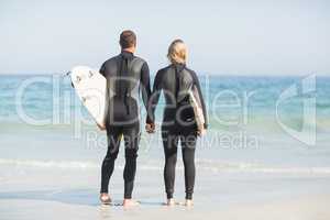 Rear view of couple with surfboard holding hand on the beach