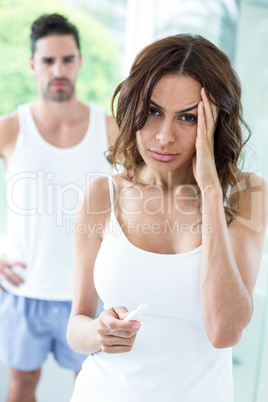 Tensed woman holding pregnancy kit while husband in background