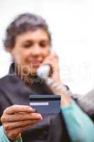Mature woman holding payment card while talking on telephone