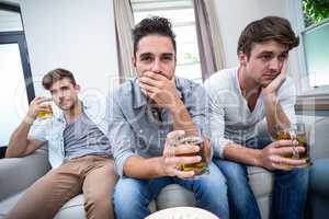 Upset male friends drinking alcohol while watching TV