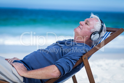 Mature man resting on a deck chair listening to music