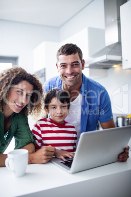 Parents using laptop with son in kitchen