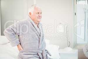 Upset senior man sitting with back pain on bed