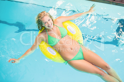 Happy woman in green bikini relaxing on inflatable tube in swimm