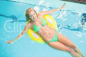 Happy woman in green bikini relaxing on inflatable tube in swimm