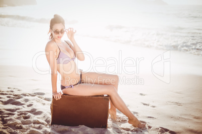 Glamorous woman in bikini sitting on an old suitcase