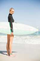 Portrait of woman in wetsuit holding a surfboard on the beach