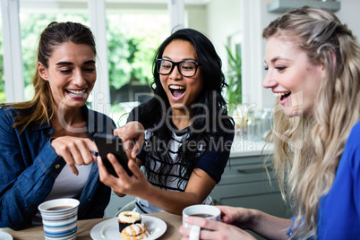 Female friends laughing while pointing on mobile phone