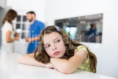 Unhappy girl looking away on table against parents