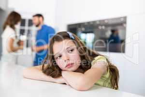Unhappy girl looking away on table against parents