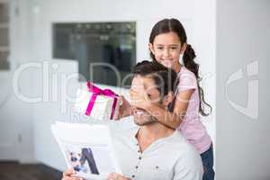 Smiling daughter covering father eyes while holding gift box