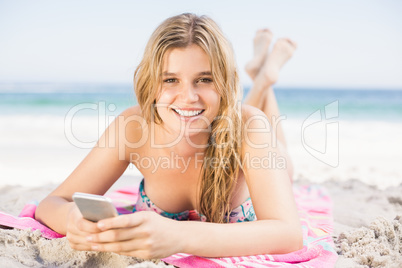Happy woman lying on the beach and using mobile phone