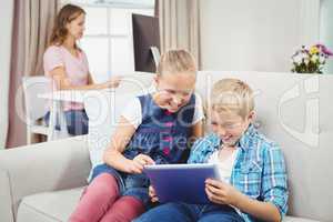 Children using digital tablet while mother in background