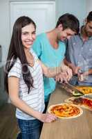 Young woman preparing pizza while friends in background