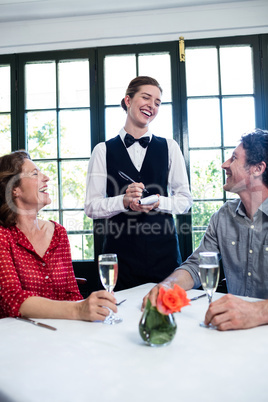 Young waitress laughing while taking an order from a couple