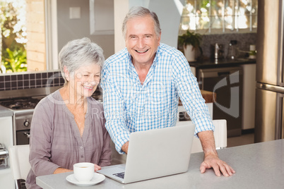 Happy senior man standing besides wife with laptop