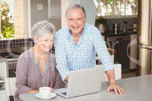 Happy senior man standing besides wife with laptop
