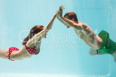 Smiling couple holding hands while swimming