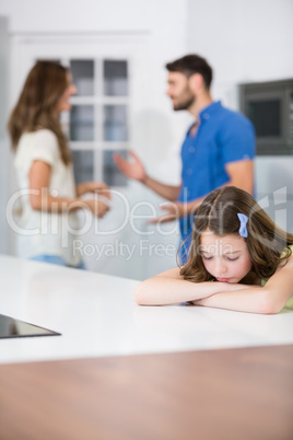 Upset girl leaning on table against parents