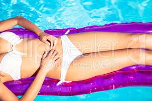 Mid section of a woman in white bikini lying on air bed in pool