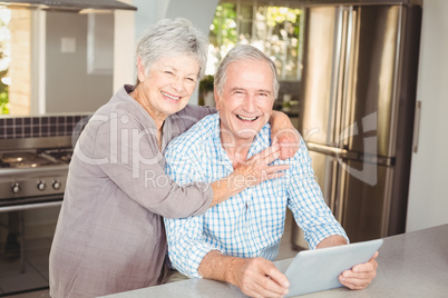 Portrait of happy senior woman embracing man with tablet