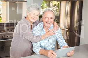 Portrait of happy senior woman embracing man with tablet