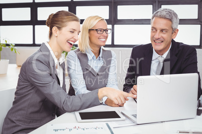 Business people smiling while discussing over laptop