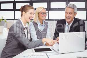 Business people smiling while discussing over laptop