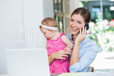 Woman talking on mobile phone while sitting with baby girl