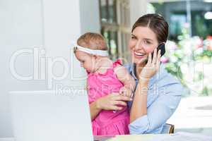 Woman talking on mobile phone while sitting with baby girl